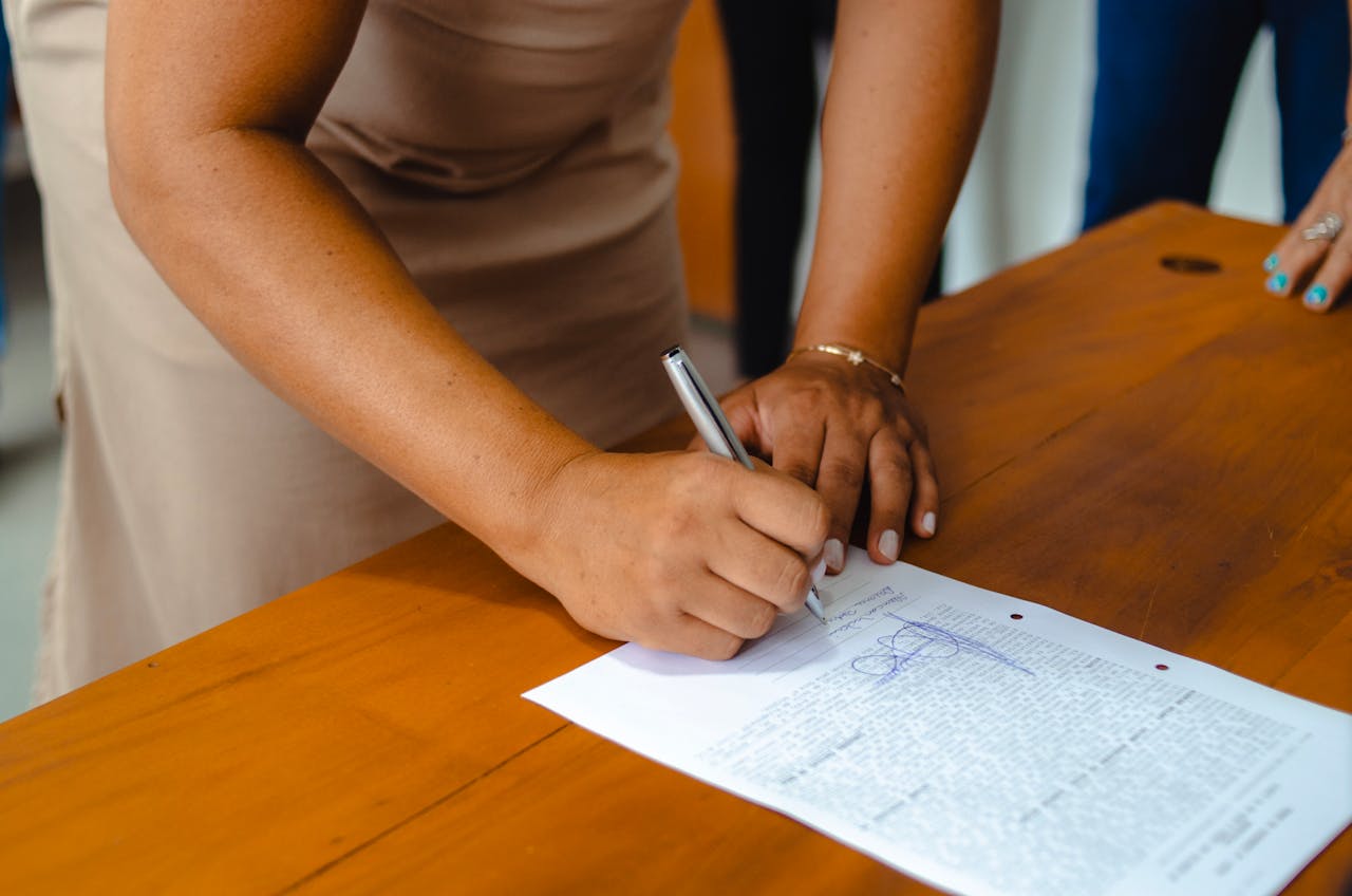 services-02 A professional woman signing an official document on a wooden table indoors.