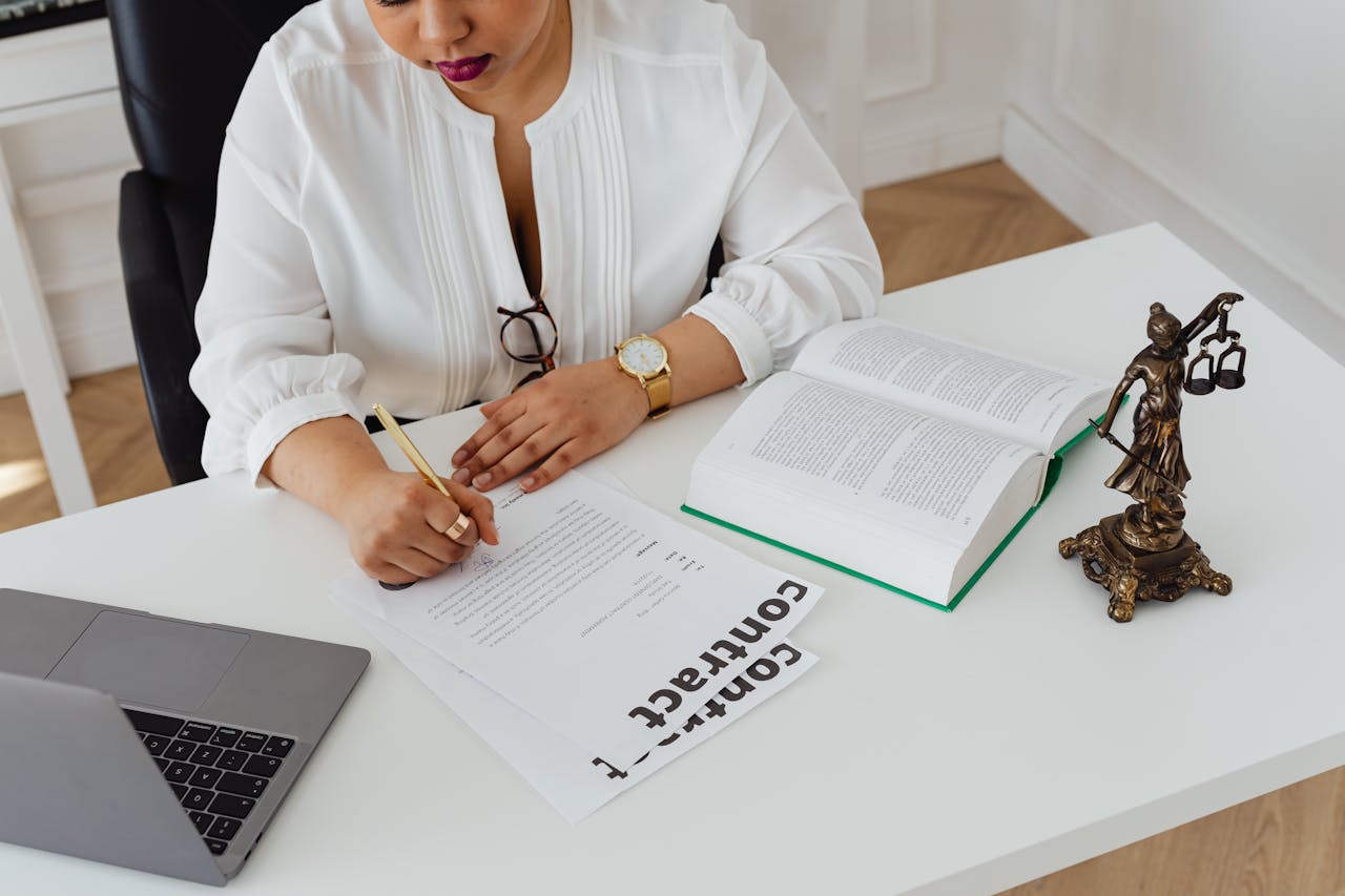 hero-img-02 Woman in office writing on contracts, with law books and laptop on table.