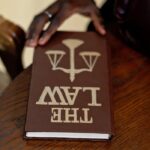 A close-up of a hand holding a law book on a wooden table, emphasizing legal studies.