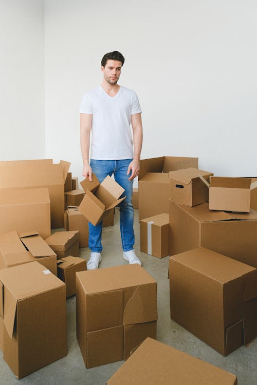 The Eviction Process Explained: A Guide for Landlords and Tenants Free Full body of exhausted young male in casual clothes standing amidst cardboard boxes and looking away pensively during relocation in new flat Stock Photo